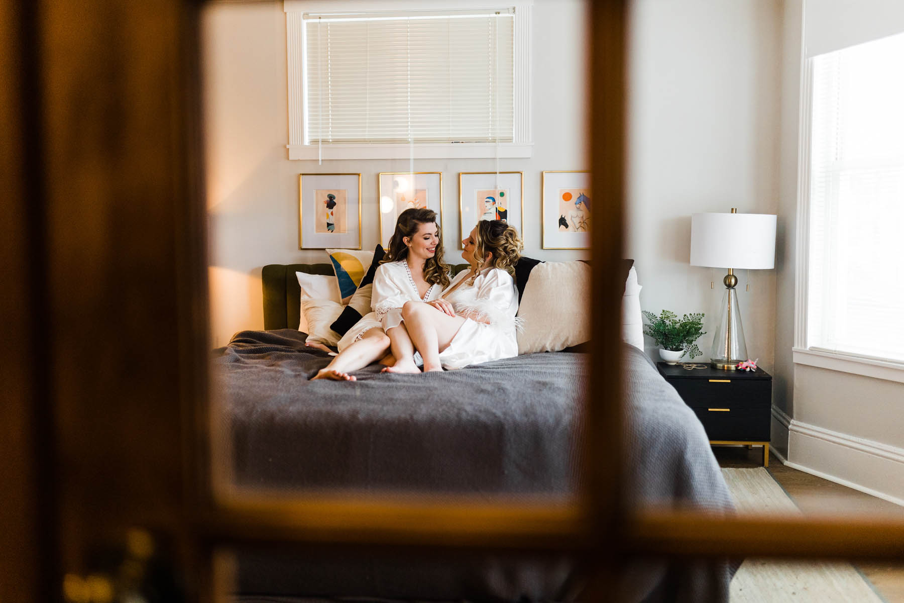 Two white people lounge on a bed as they get ready for their wedding.