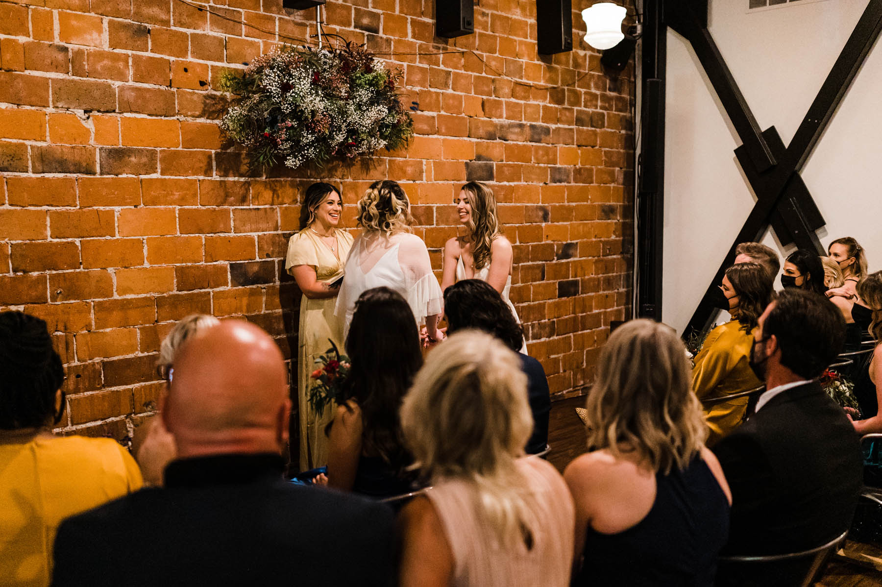 Two people stand in front of their attendants in a brick building, exchanging vows.