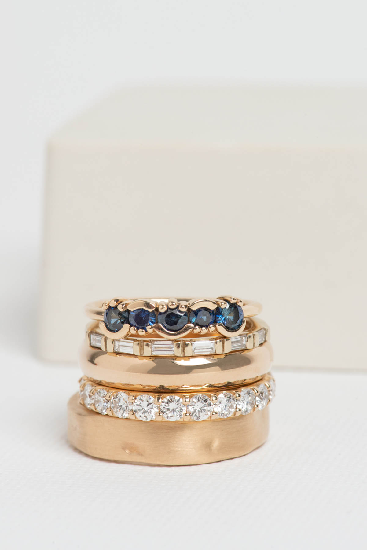 A stack of rose gold rings with blue and silver accents.