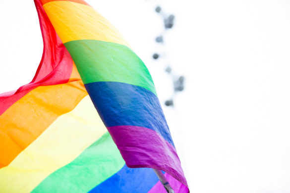 A rainbow flag blows in the wind against a white background.