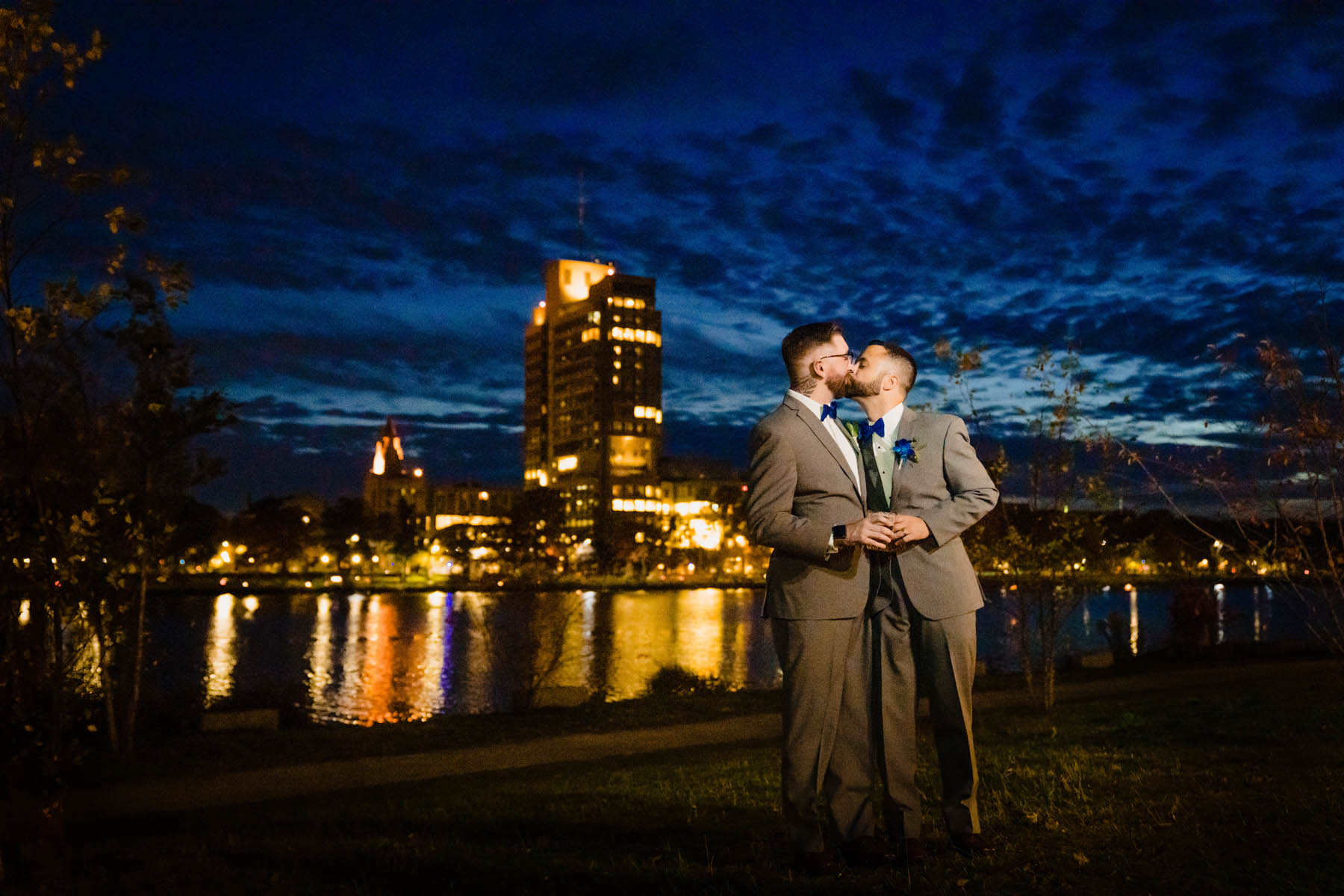 The newlyweds share a kiss in front of the Boston skyline with a royal blue sky behind them.