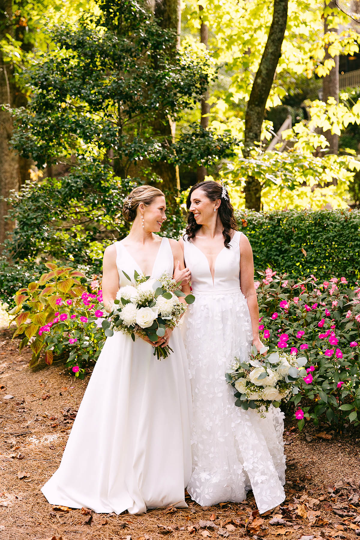 Two brides stand side by side and hold bouquets of white flowers.
