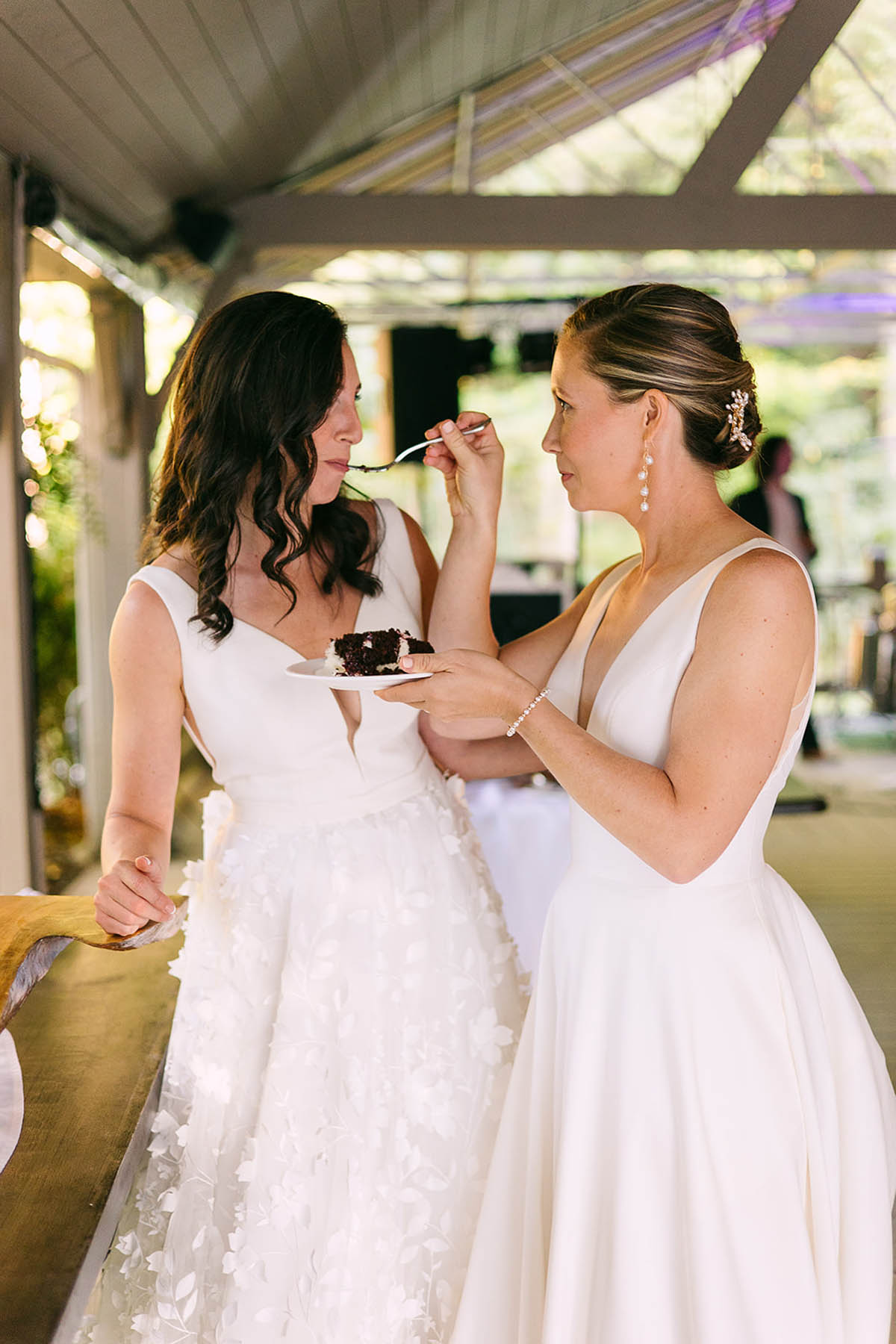 A blonde bride feeds a bite of wedding cake to her new wife. 