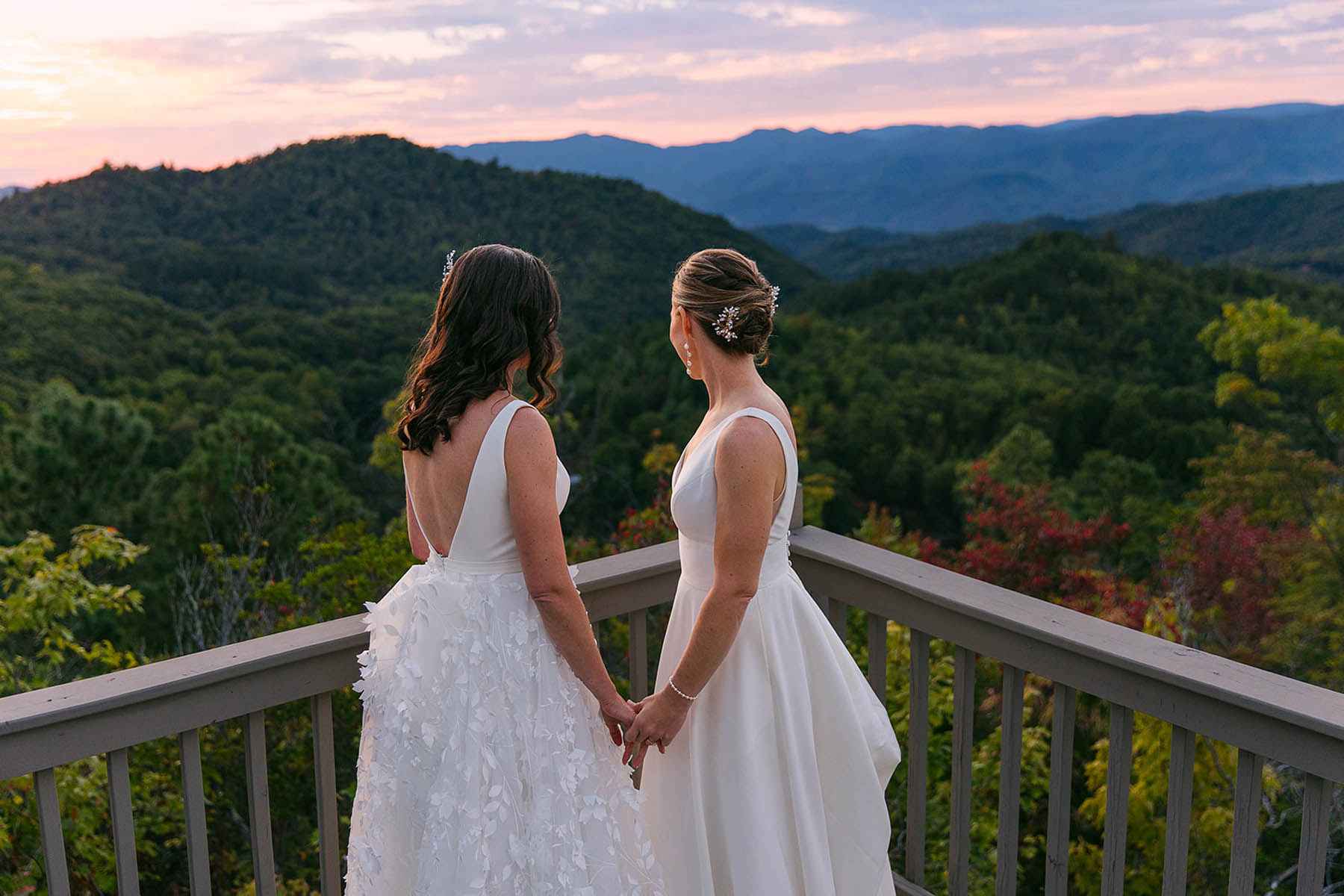 Two brides stand on a balcony and look out at the North Carolina mountains.