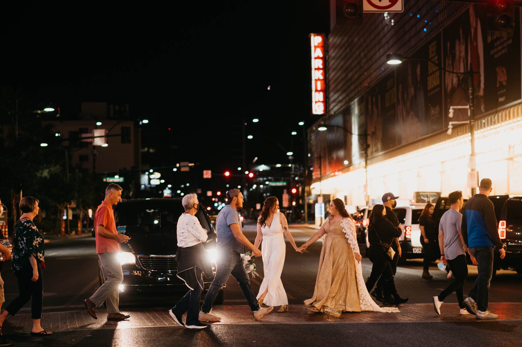 The newlyweds walk across a Las Vegas street at night with a red Parking sign in the background. 