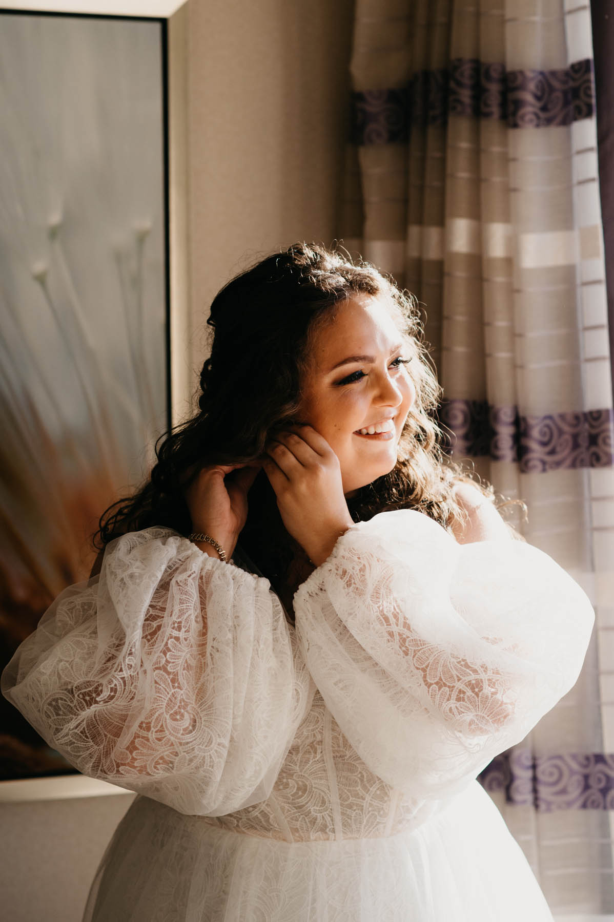 A white brunette gets ready for their wedding in front of a sunny window.