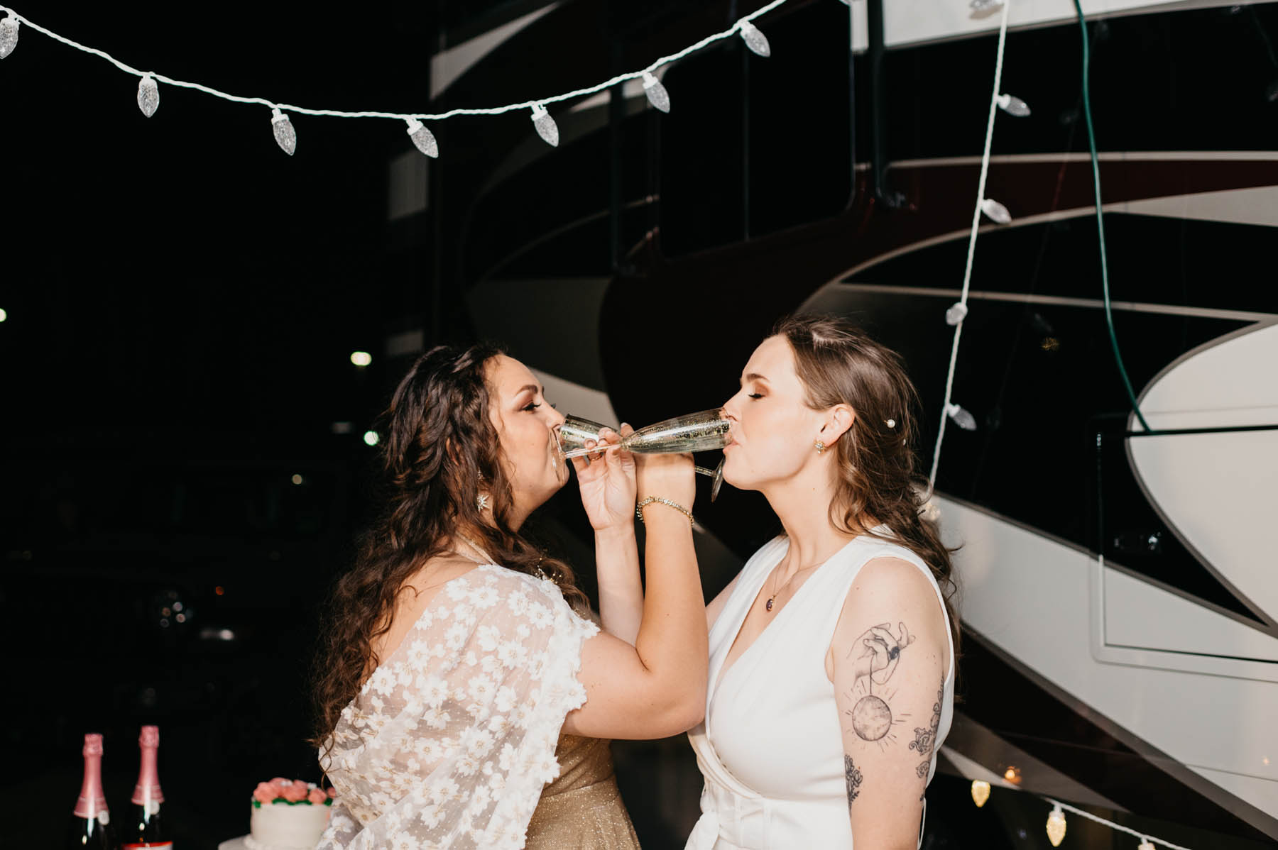 The newlyweds intertwine their arms and sip champagne in front of a black and white RV.