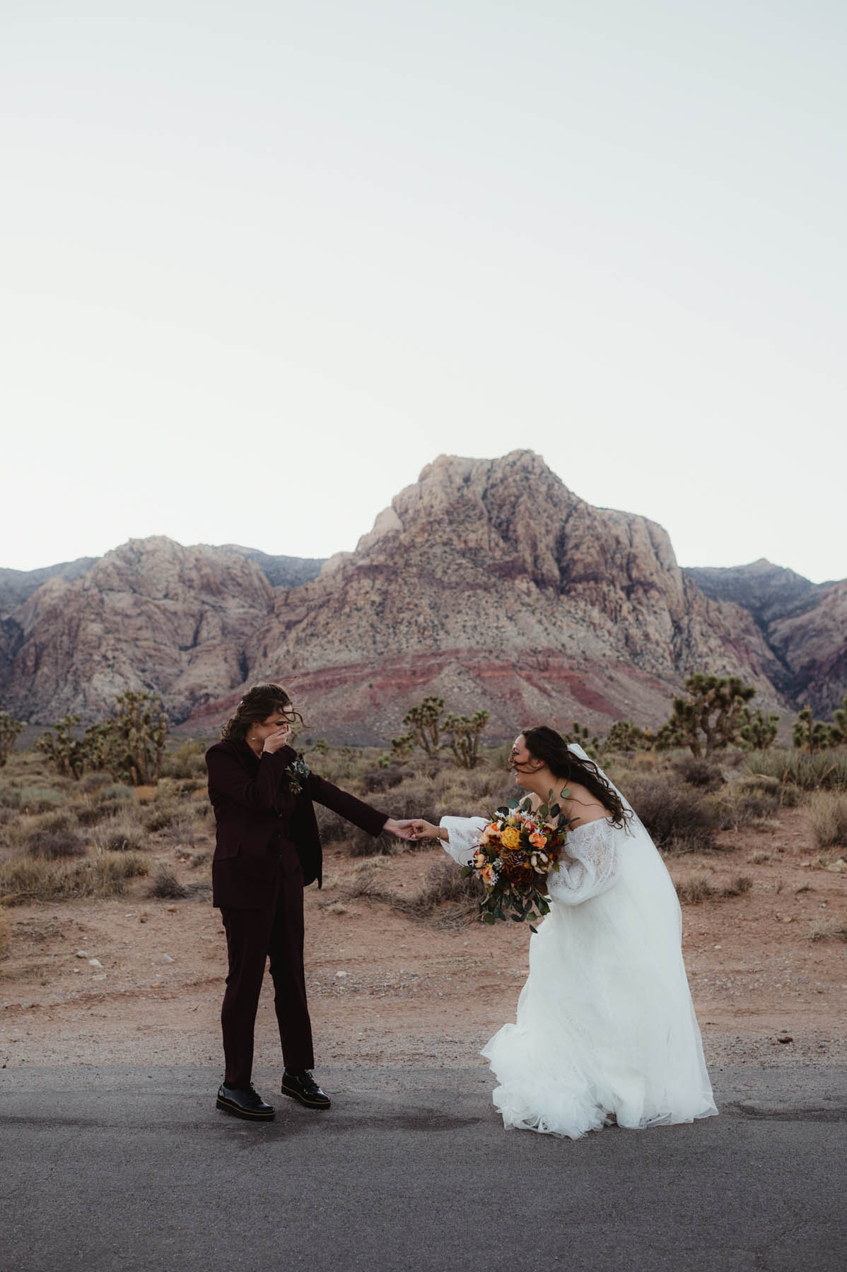 A first look of two white brunettes holding hands in a desert.