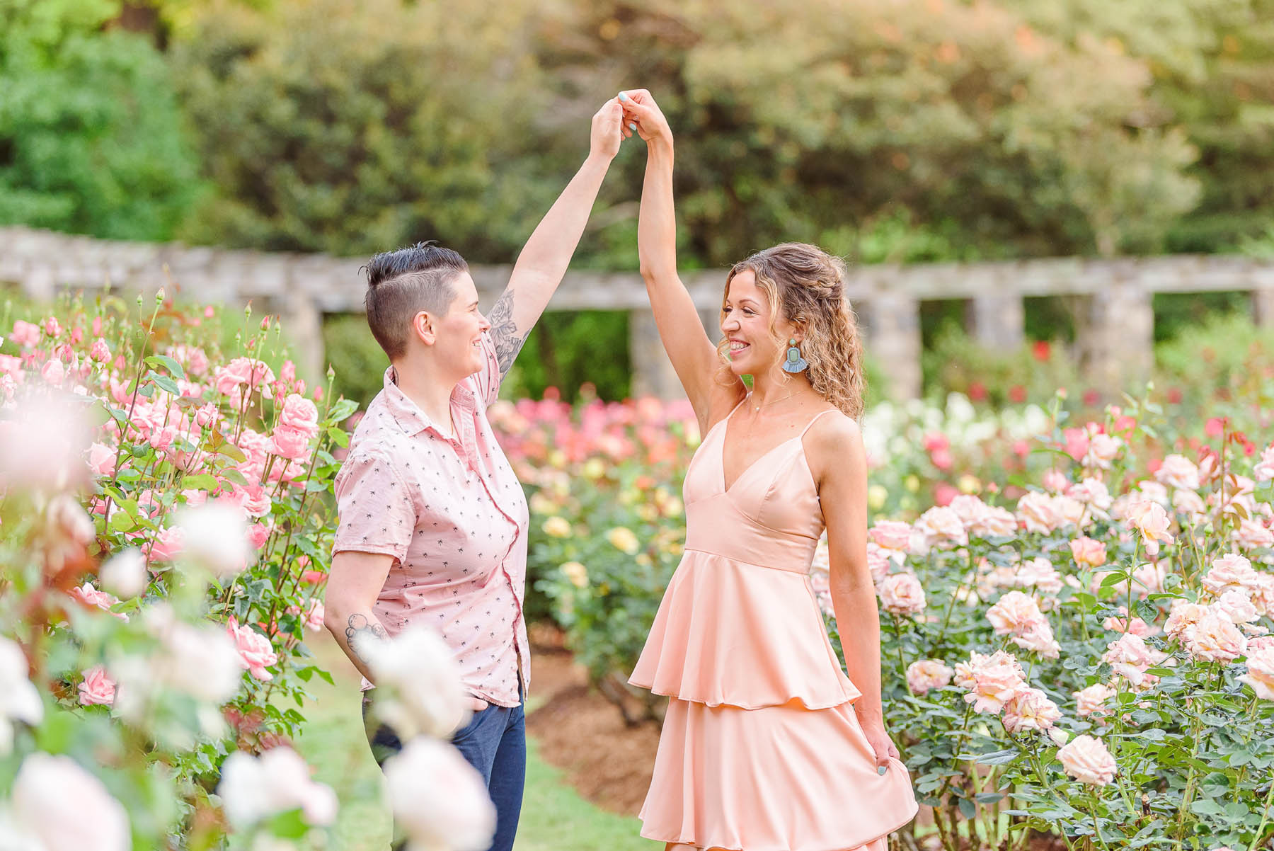 Two white people dressed in pink hold hands in a botanical garden.