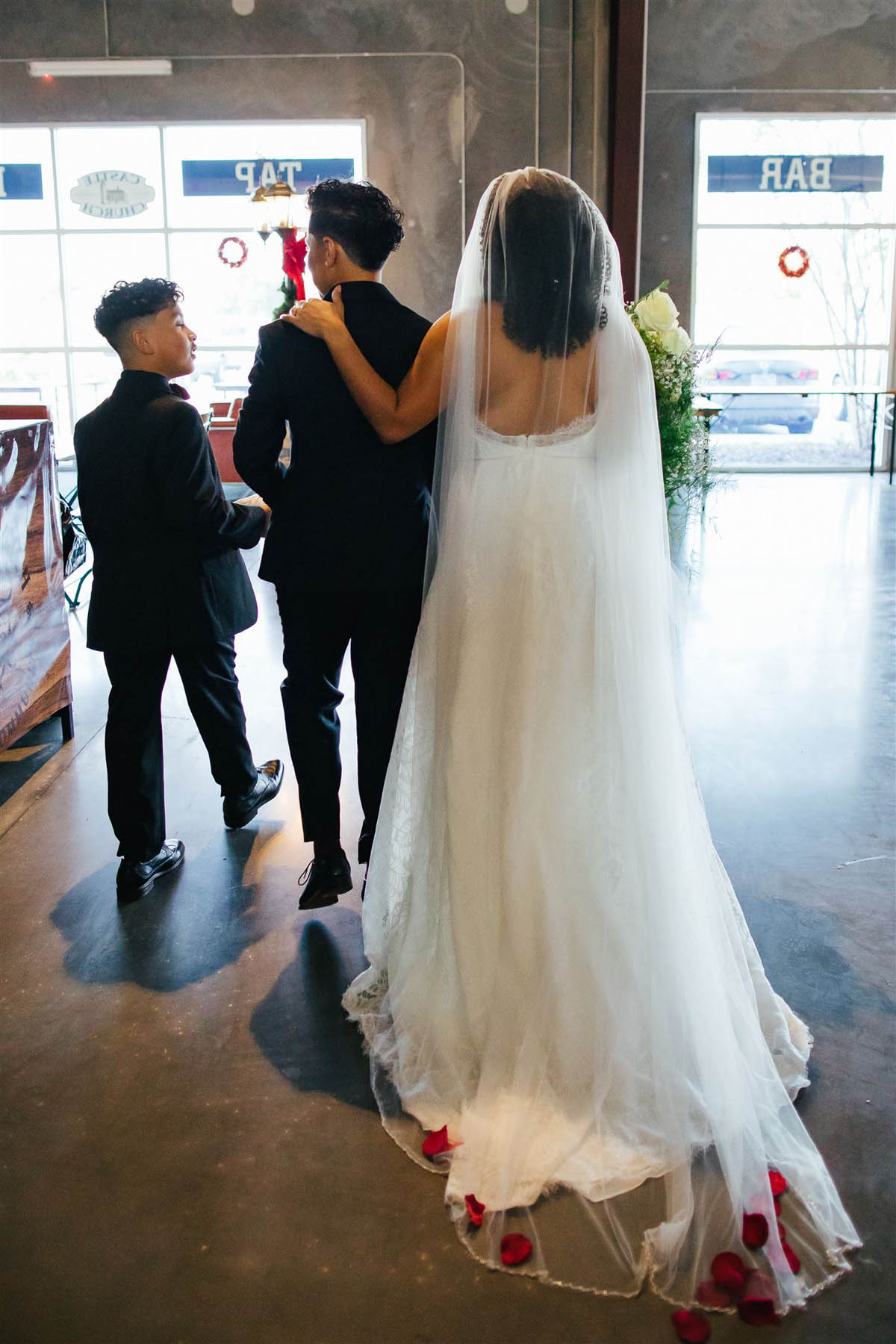 Two brides and their son stand together, walking down an aisle.