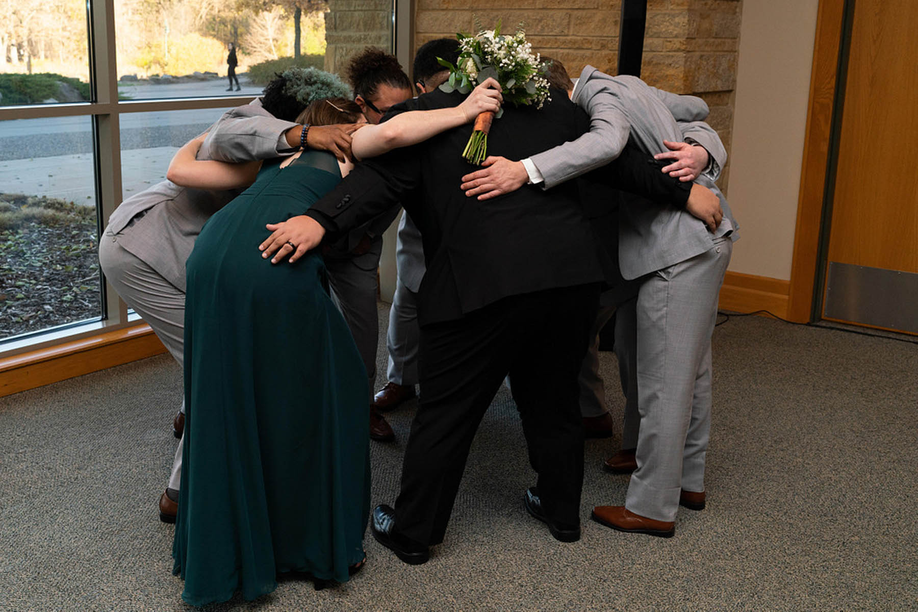 A group of people in black, green and gray huddle on the side of a wedding ceremony, like a rugby team.