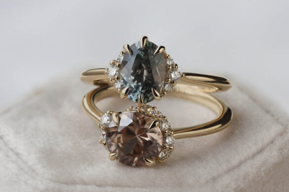 Two rose gold rings with dusty pink and blue gemstones sit on top of a closed pink jewelry box