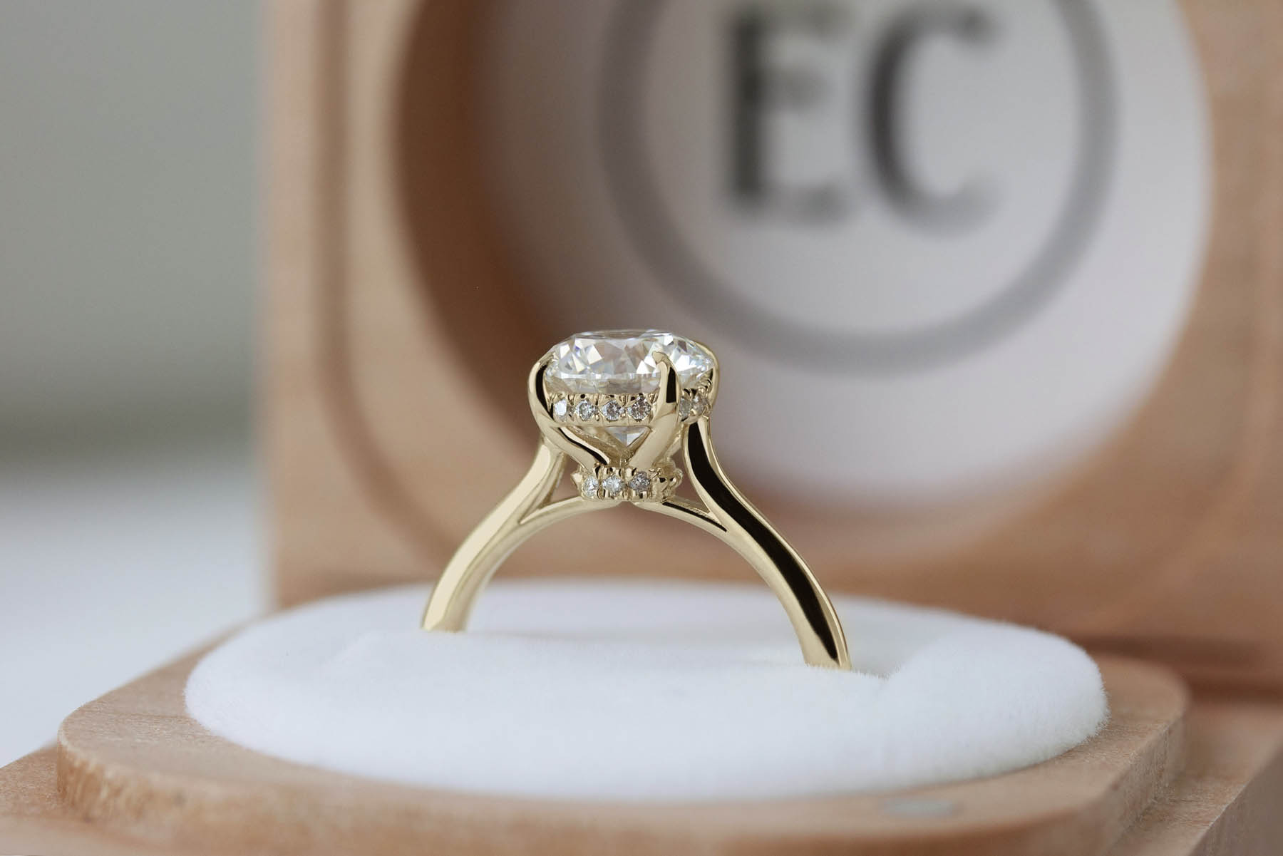 A close-up sideways shot of a gold band ring with a hidden halo and clear gem, siting up in a jewelry box.