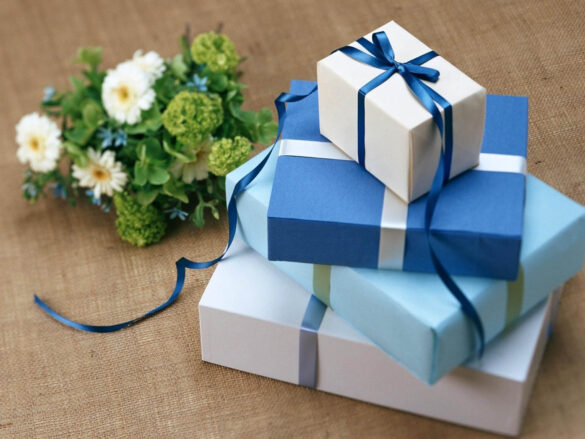 A pile of blue and white gift boxes sit on a beige surface next to a bundle of white flowers.