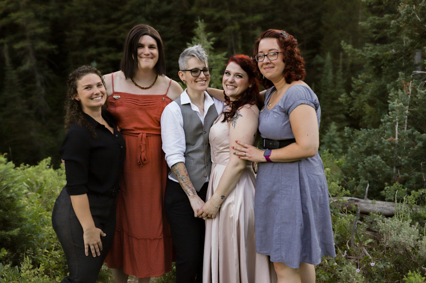 Two brides (both white, one with short gray hair, one with long dark red hair) stand with their chosen family at their outdoor wedding