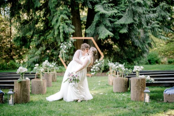 White lesbian bride kisses her new wife while dipping her with a magical forest scene in the background
