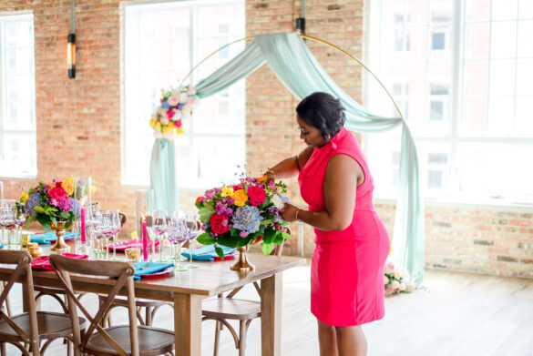 Chicago wedding planner Qiana Turner, a Black woman in a pink dress, sets table for wedding reception using hot pink wedding colors.
