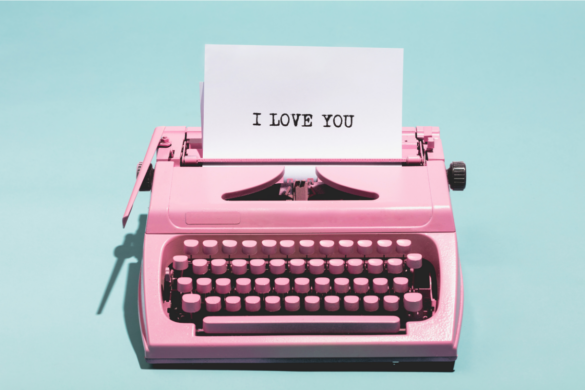 Aqua background with pink typewriter with a piece of white paper with the words "I love you" typed on it.