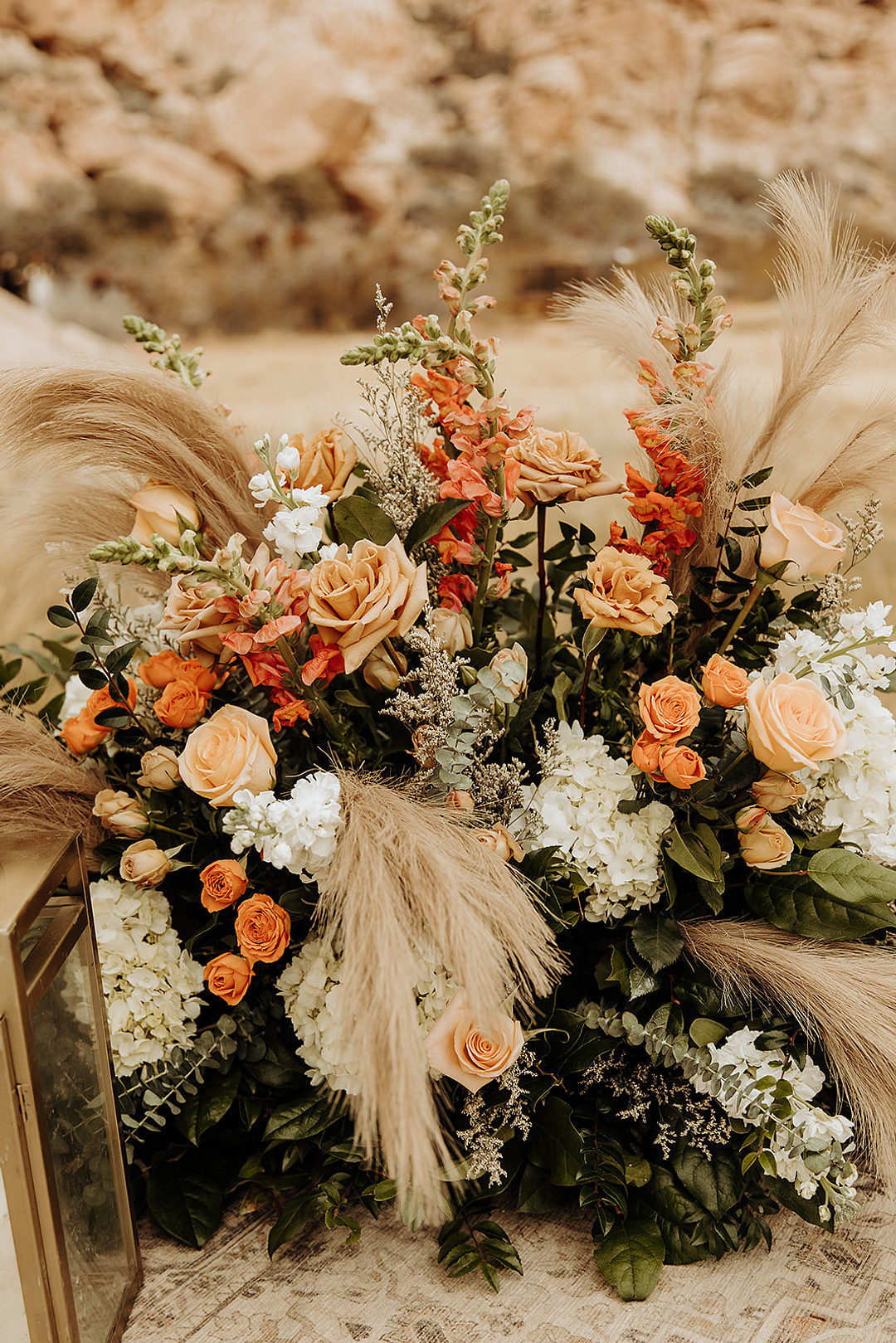 Floral arrangement of white and peach roses, coral orange gladiolas, orange leaves, eucalyptus leaves and pampas grass for an outdoor wedding in a desert.