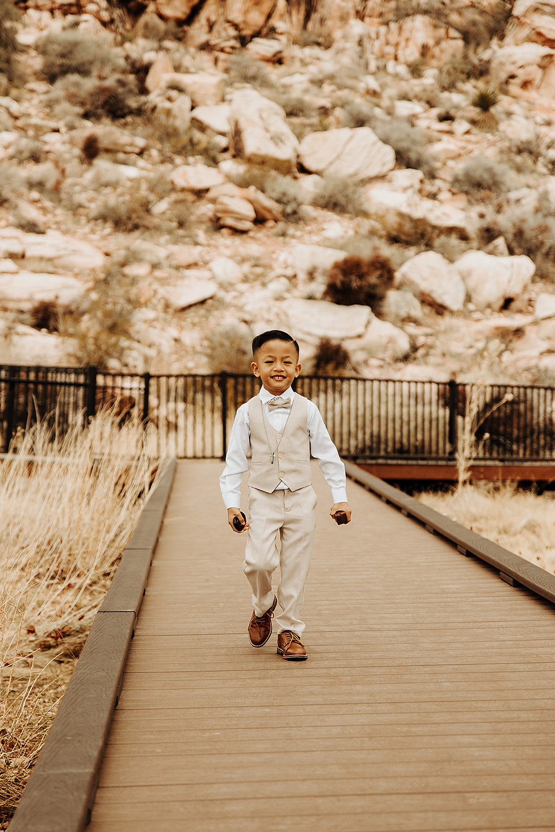 Ring bearer at outdoor wedding wearing a light tan vest, bow tie and pants.
