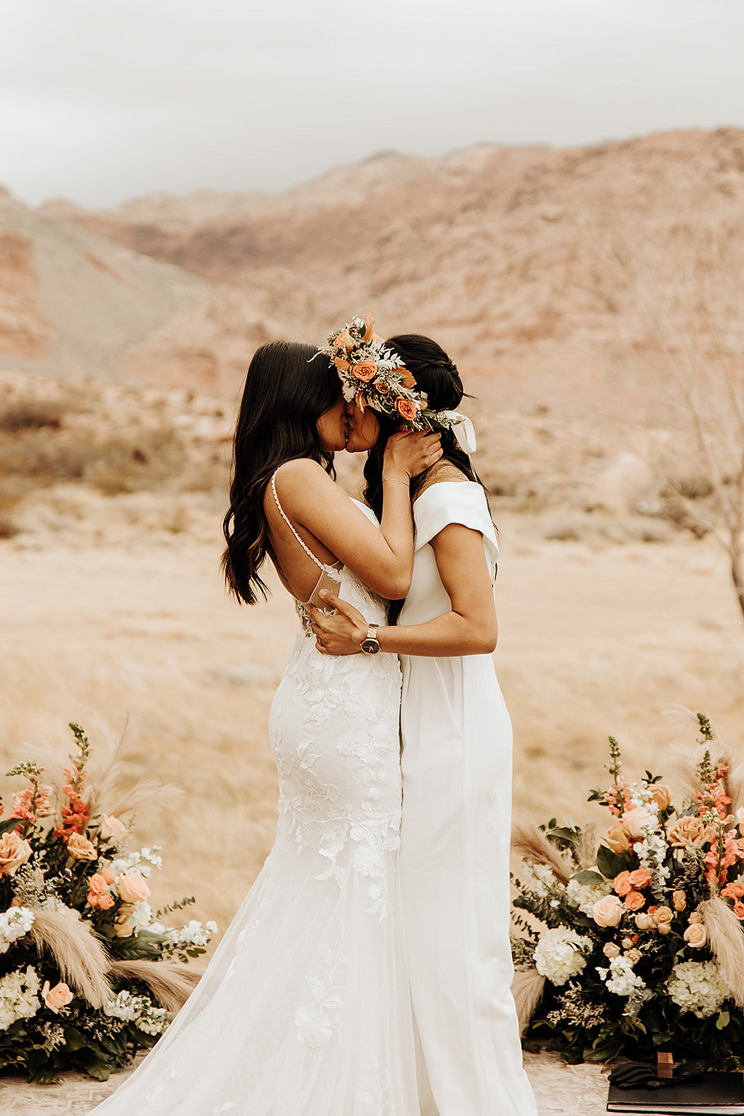 Two brides kiss and embrace at their outdoor desert wedding.