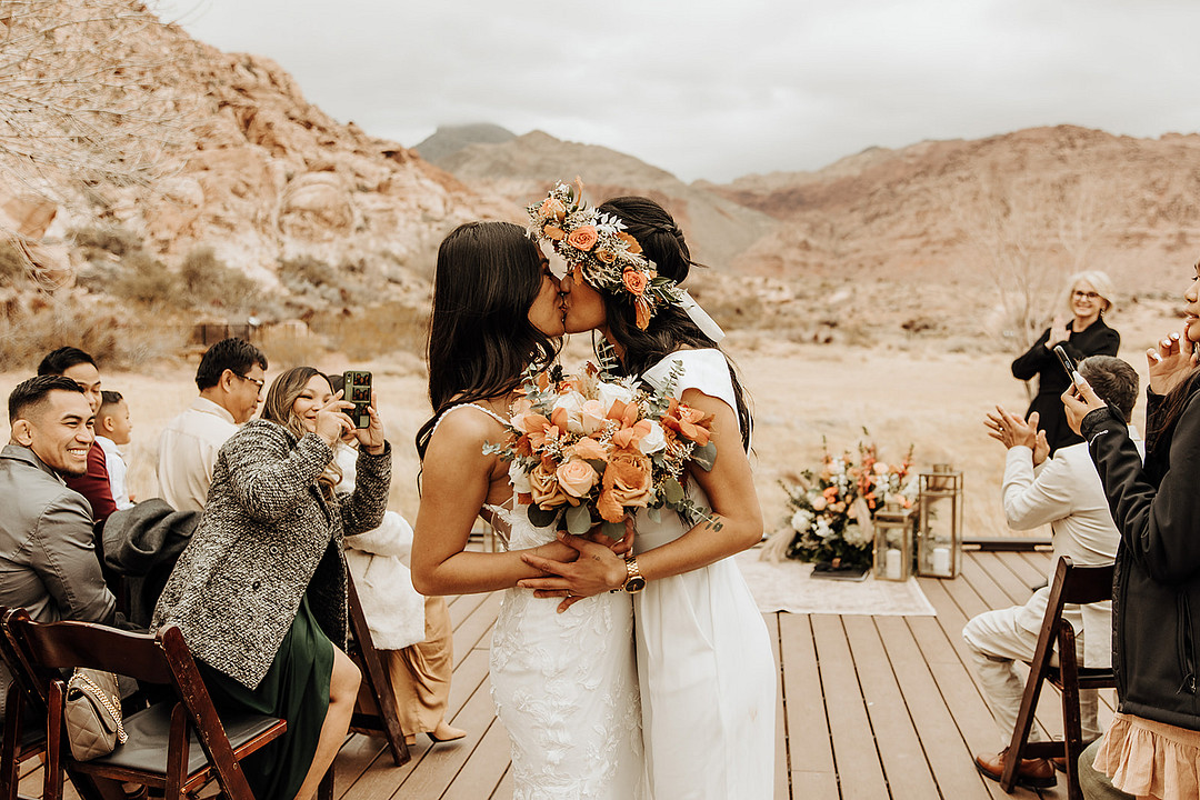 Lesbian wedding at intimate Red Rock Canyon elopement. The brides are kissing and the family is clapping.