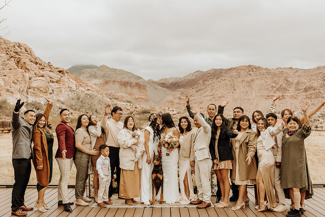 Lesbian wedding at intimate Red Rock Canyon elopement. The whole family is in the wedding portrait and they are holding their hands in the air and smiling.