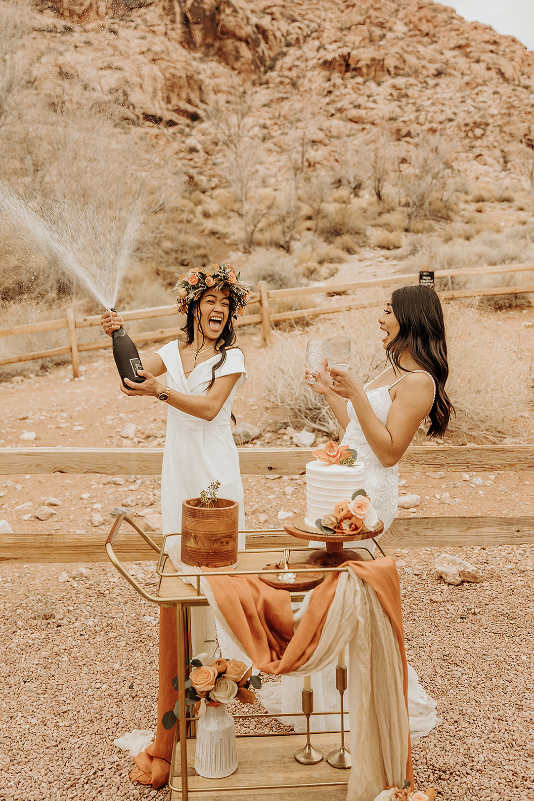 Two brides celebrate their wedding in Red Rock Canyon with champagne and cake.