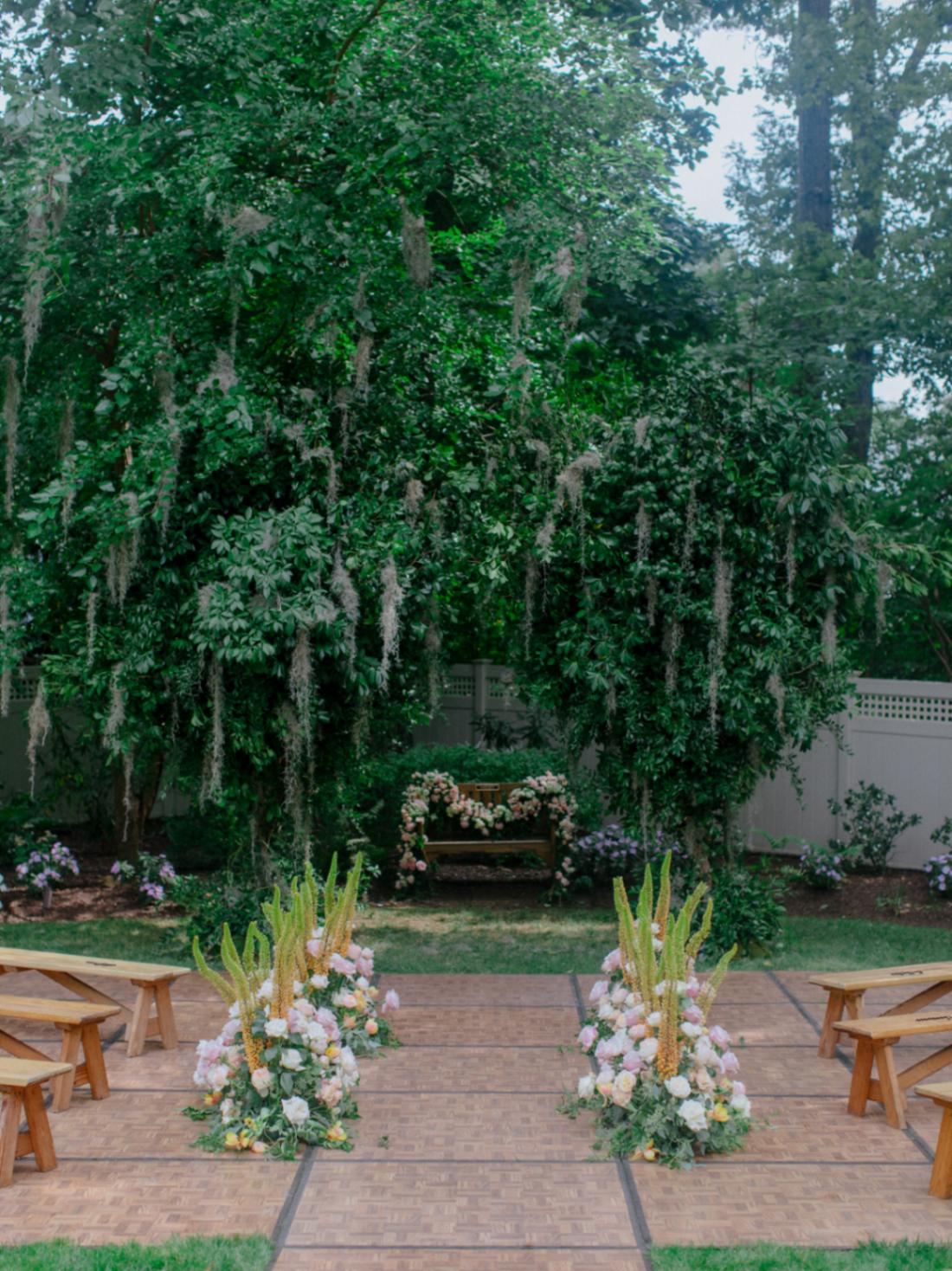 Outdoor wedding ceremony set up with wooden benches, a prayer bench, two mossy oaks | Photo by Chris J. Evans
