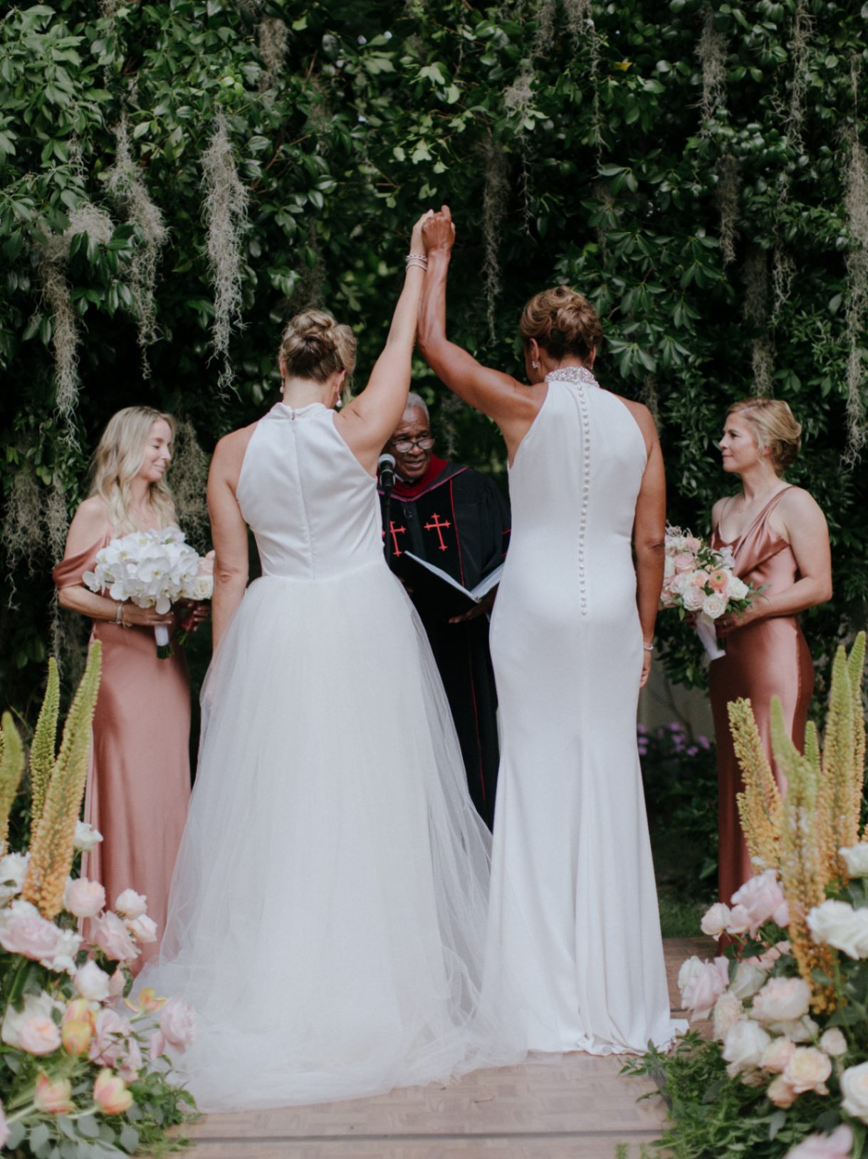 Robin Roberts and Amber Laign, a celebrity lesbian couple, hold up their hands together during their wedding. The brides are wearing white Badgley Mischka wedding gowns.