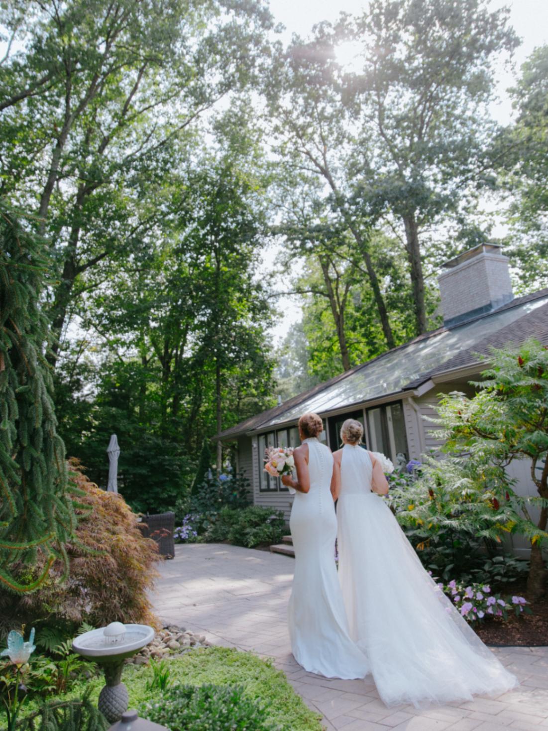 Robin Roberts and Amber Laign, a celebrity lesbian couple, walk on a gray brick path in their Badgley Mischka wedding gowns.