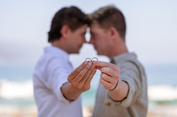 Two white men in love hold out their hands showing off their engagement rings