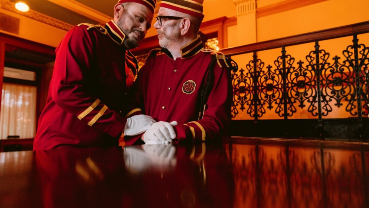Two white men with deadly face paint and wearing red bell hop uniforms