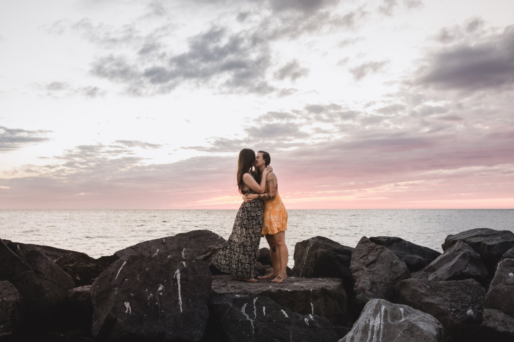 two women in love holding each other while standing and kissing on beach rocks