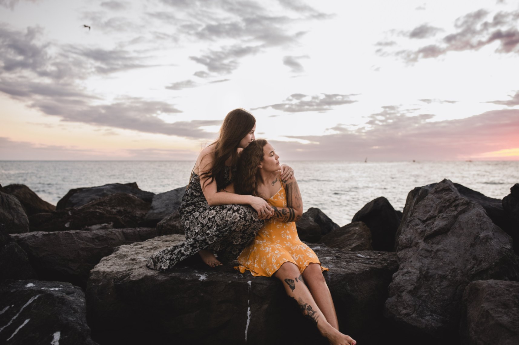 two women in love holding each other while sitting on beach rocks