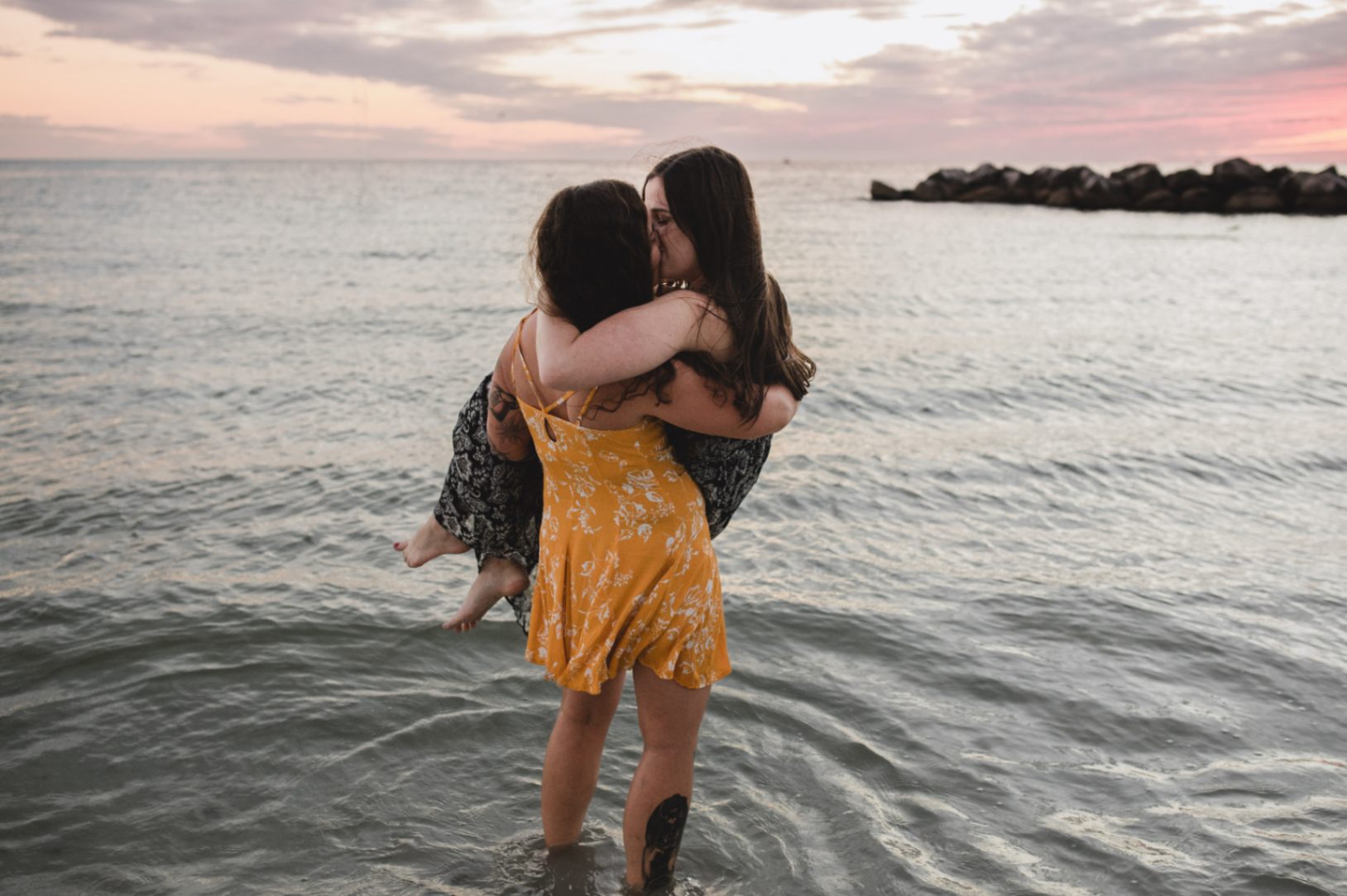 one brunette woman holding another while kissing in the water