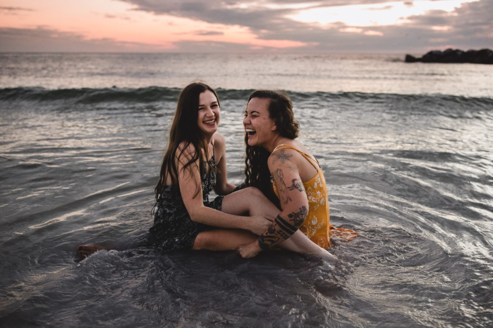 lesbian women wrapped up in each other sitting in the ocean laughing