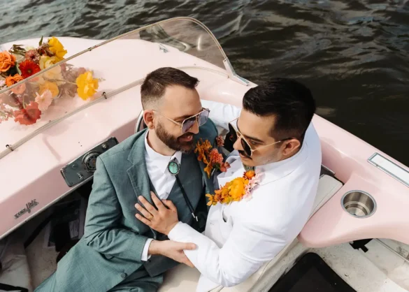Two grooms laying on each other in a pale pink boat with red and orange flowers