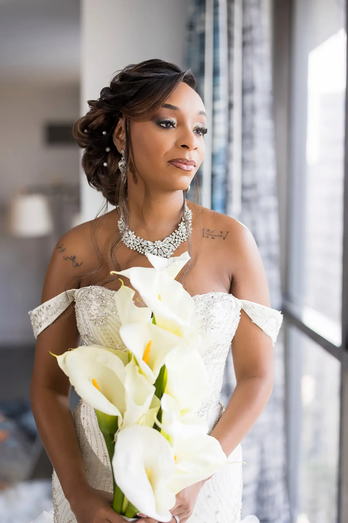 Black bride Daniella in off-shoulder beaded wedding gown holding white calla lily bouquet