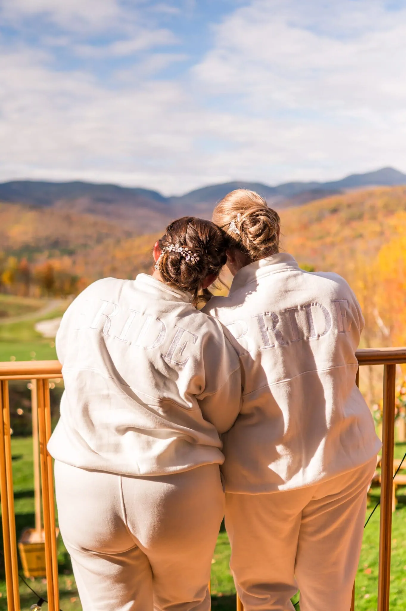 A white lesbian couple leaned on each other with their backs to the camera. They face the mountains.