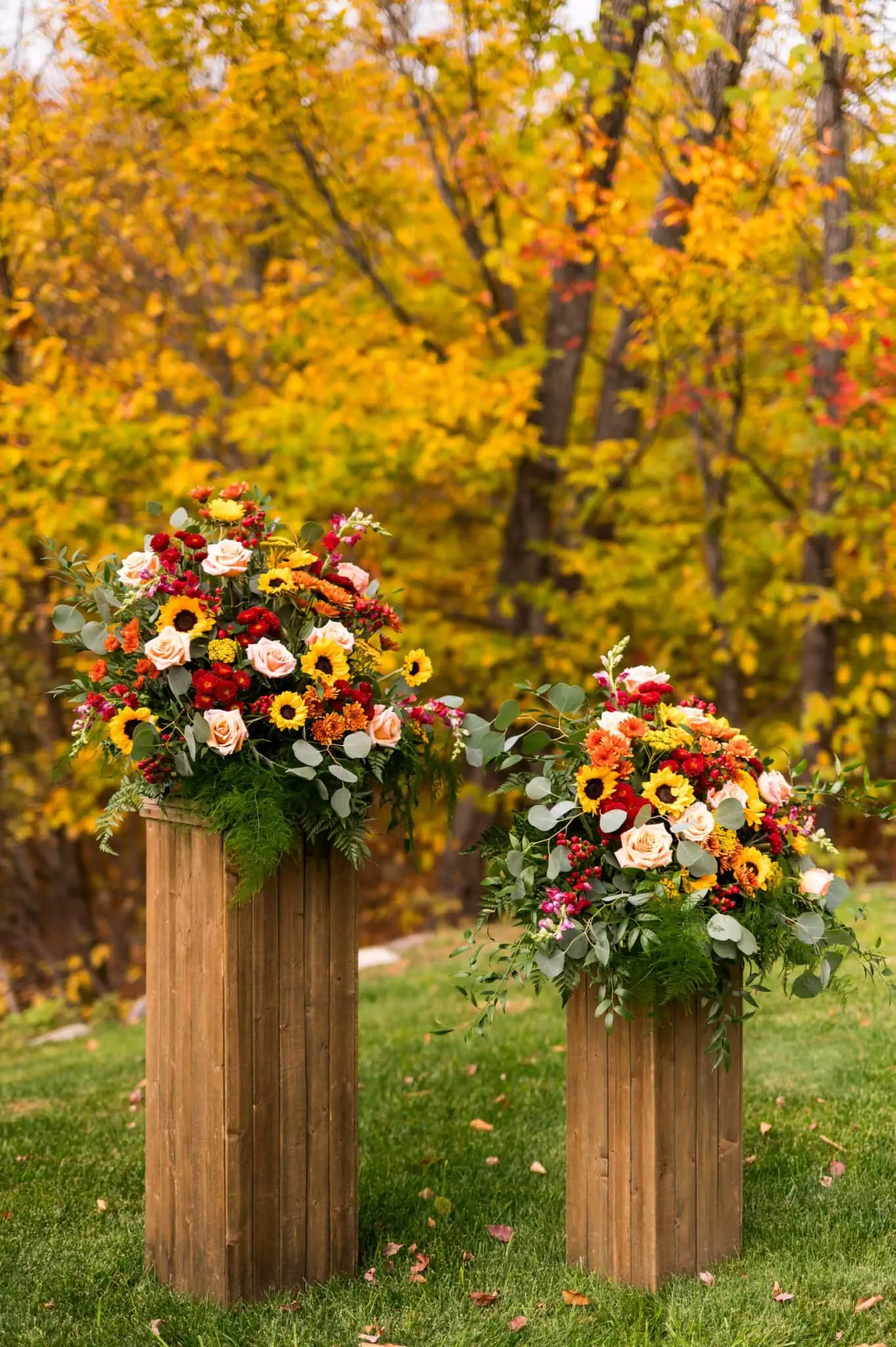 Autumn flowers on a wooden pedestal featuring sunflowers, bronze mums and burgundy amaranth for an autumn mountain wedding