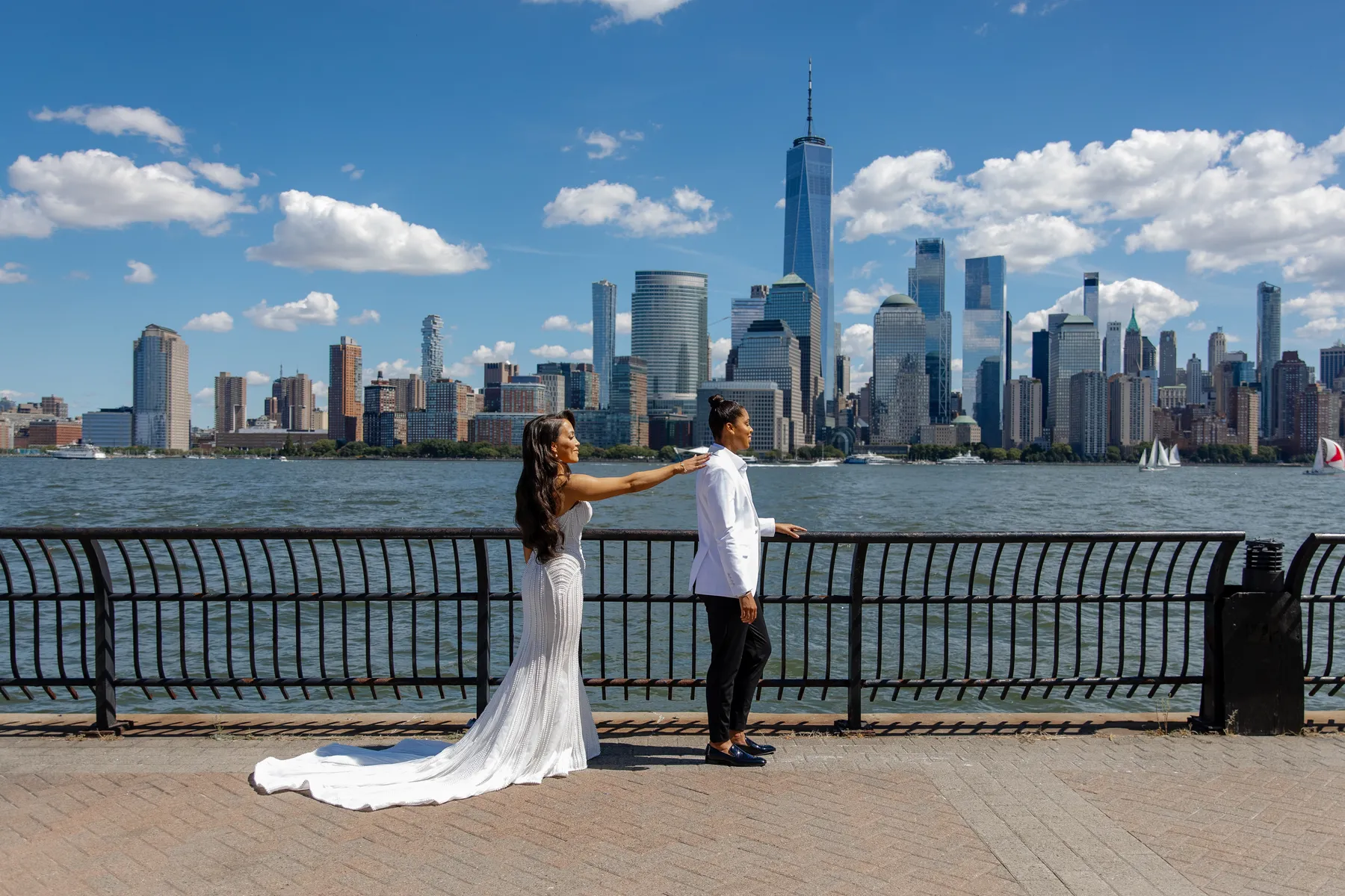 Katherine and Michelle pose along the Hudson River waterfront with the Manhattan skyline behind them on their wedding day.