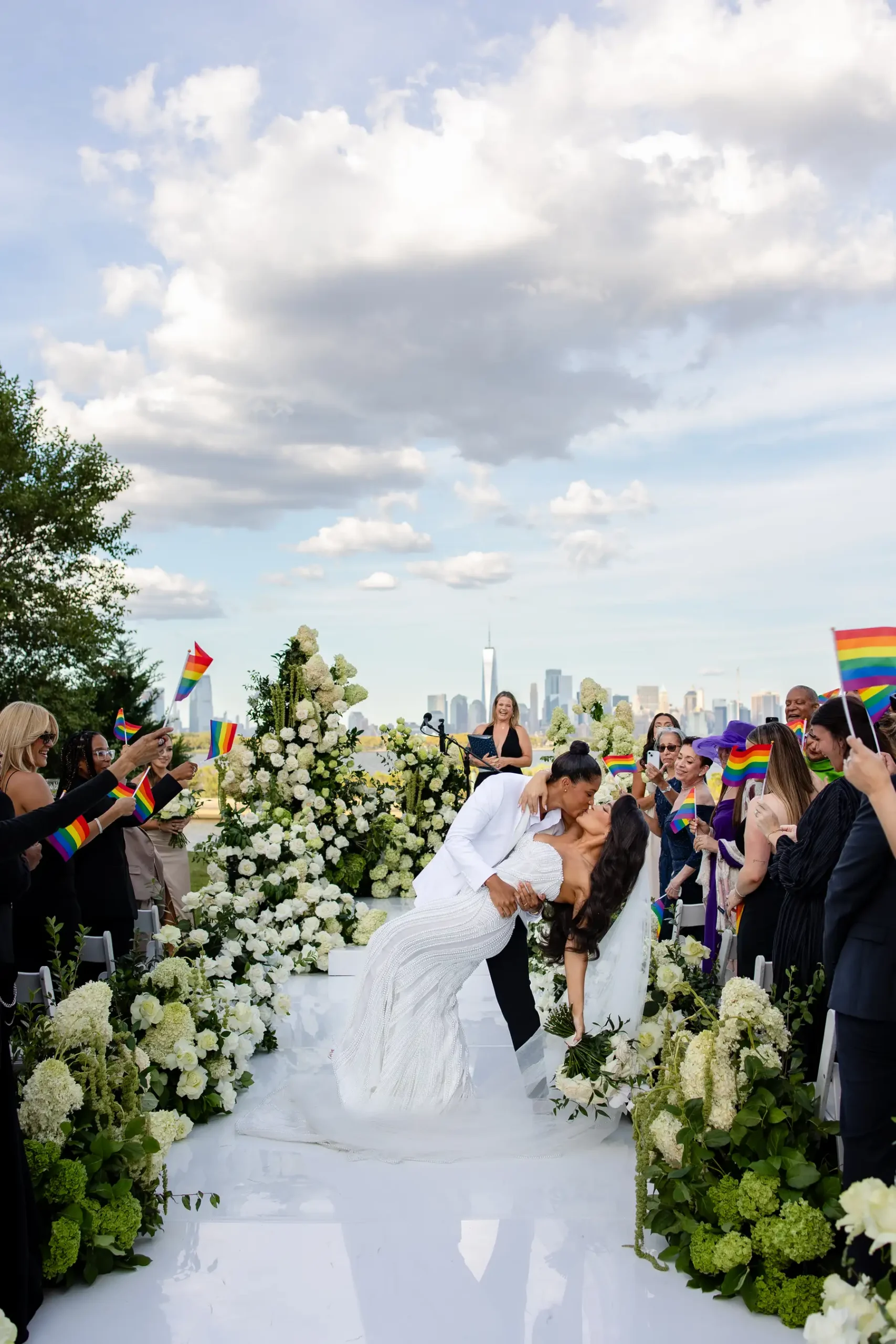 Katherine and Michelle share a dip kiss at Hudson House in Jersey City as guests wave rainbow Pride flags.