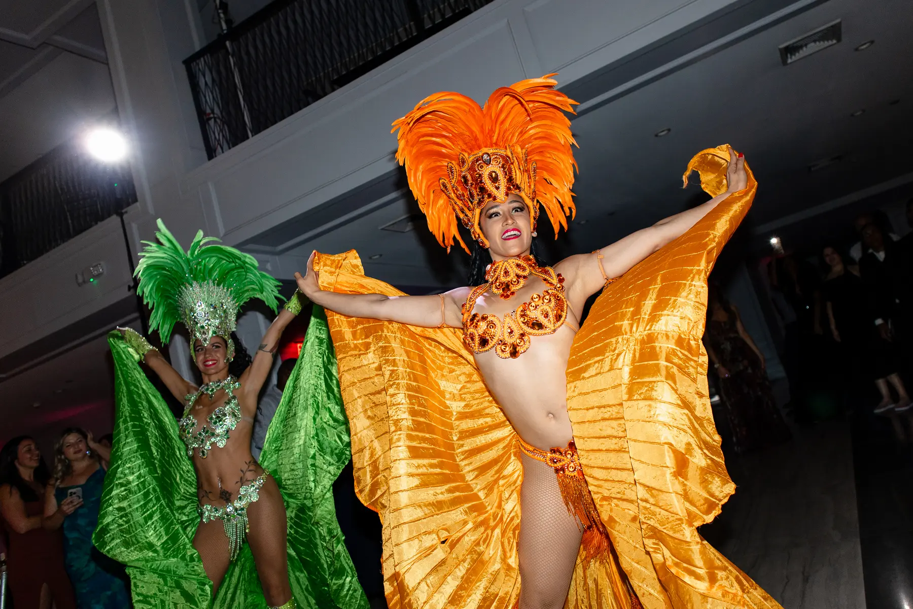 Samba dancers in vibrant orange and green carnival costumes perform at Katherine and Michelle's wedding at Hudson House.