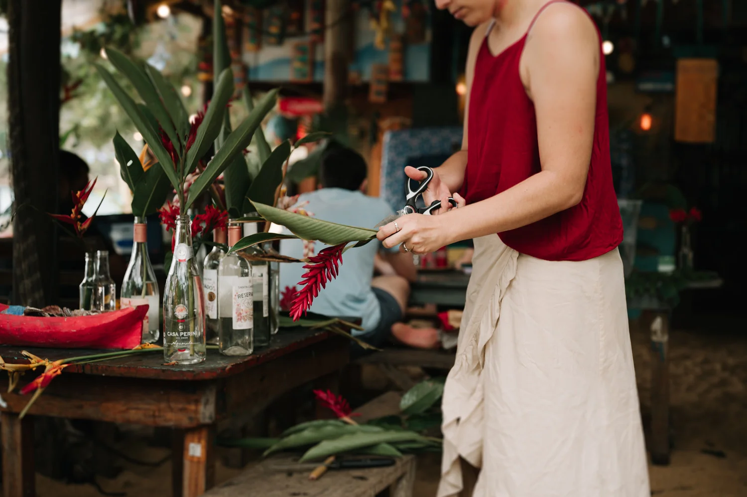 A woman in a red top trims tropical flowers into repurposed glass bottles at Pouso das Flores in Paraty, Brazil.