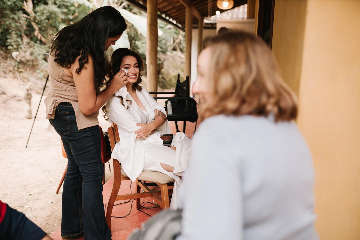 Bride Rafaela smiles as a makeup artist dabs her face during wedding prep at Pouso das Flores in Paraty, Brazil.