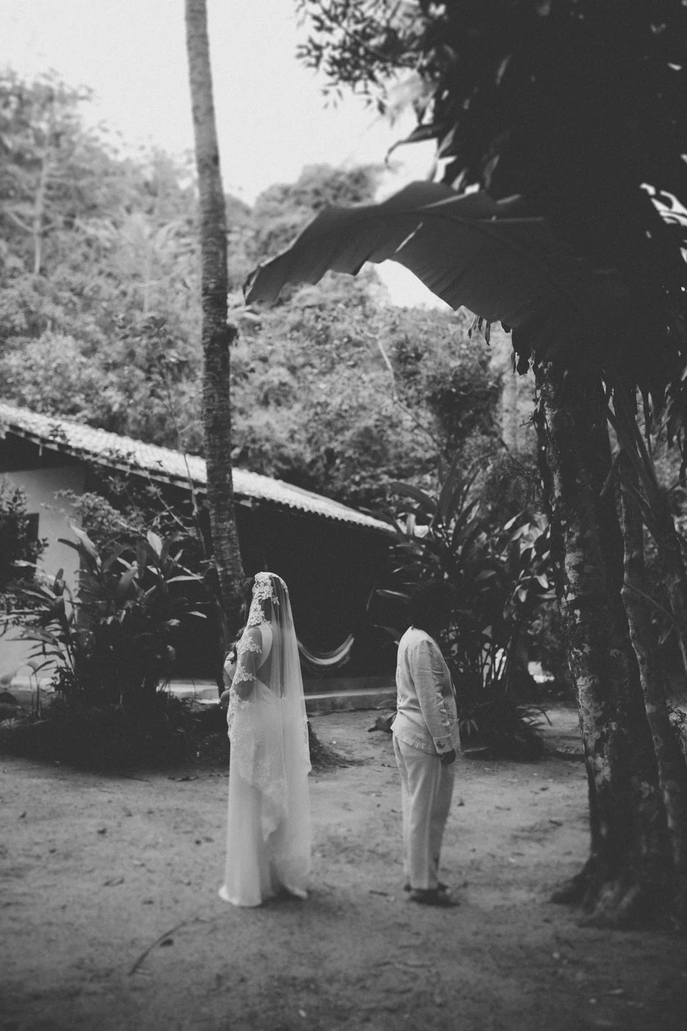 Rafaela and Nathalia stand with their backs to the camera in a lush garden at Pouso das Flores in Paraty, Brazil.