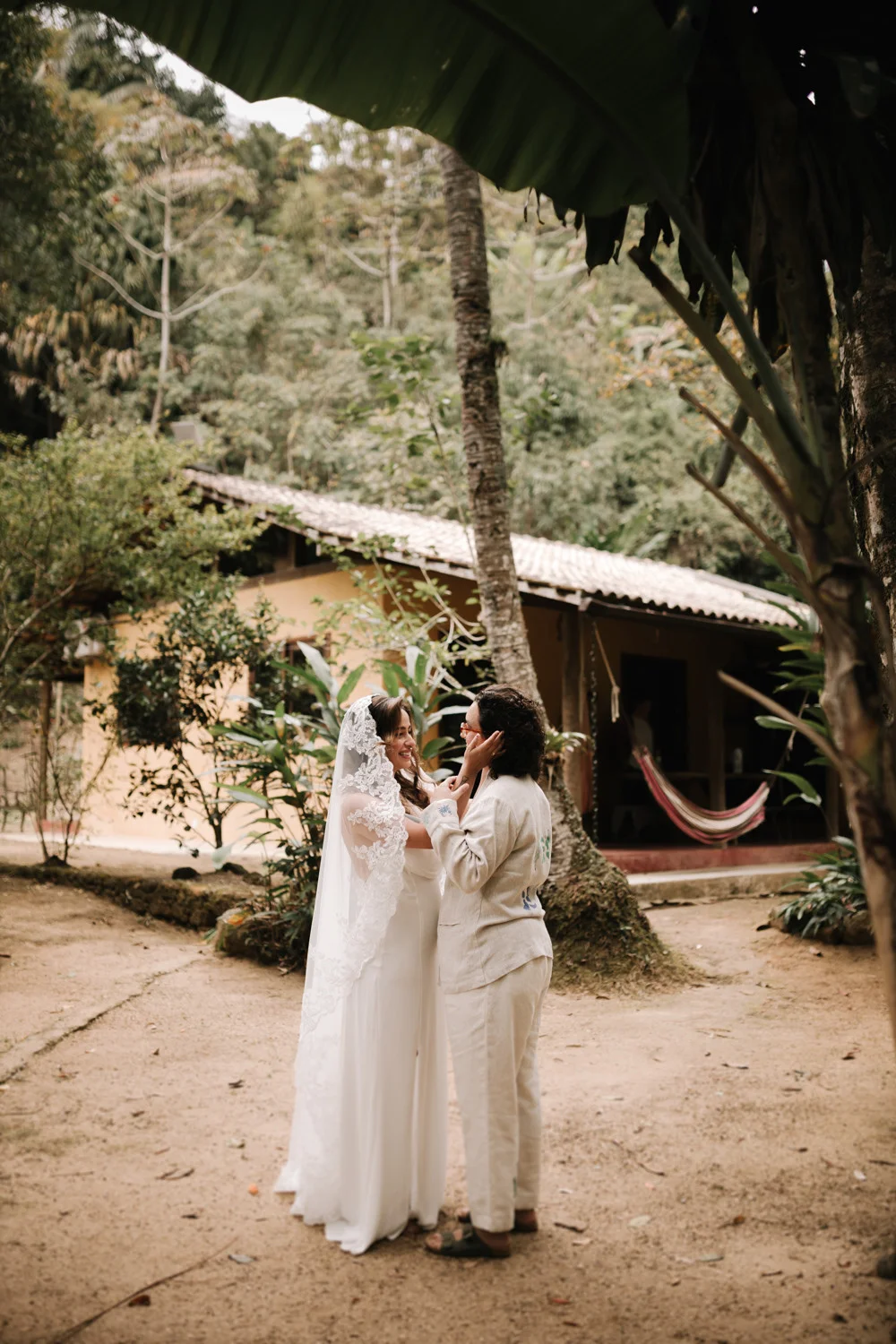 Rafaela and Nathalia share a tender moment in their wedding attire amid lush greenery at Pouso das Flores in Paraty, Brazil.
