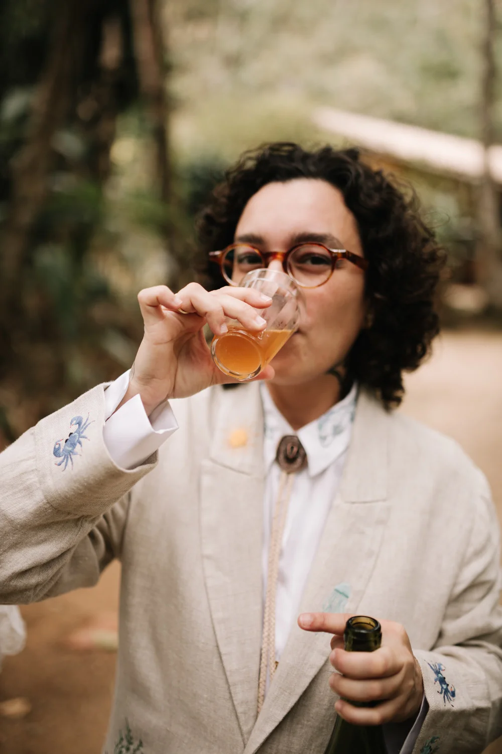 A wedding guest in a linen blazer sips from a small glass at Pouso das Flores in Paraty, Brazil.