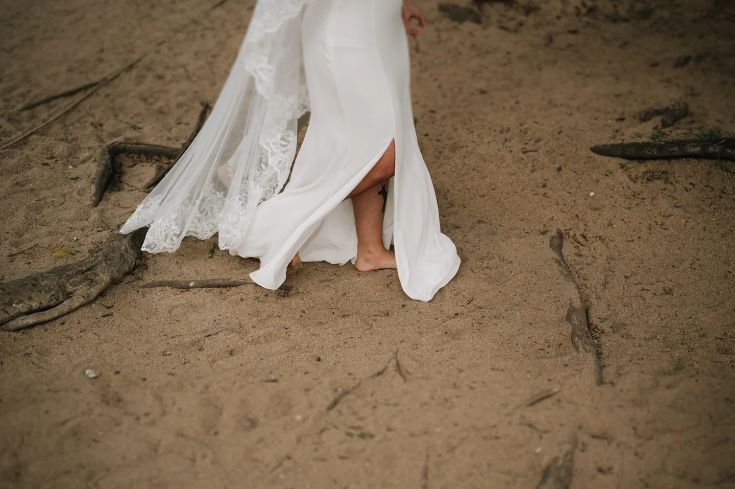 Barefoot bride in flowing white lace gown walks on sandy beach at Pouso das Flores in Paraty, Brazil.